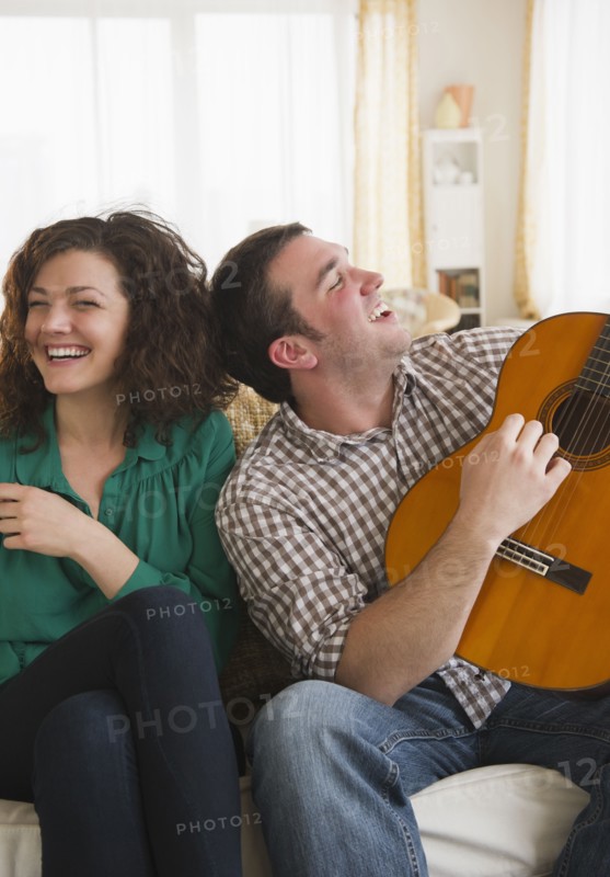 Couple sitting on sofa, man playing guitar. 
Photo: Jamie Grill