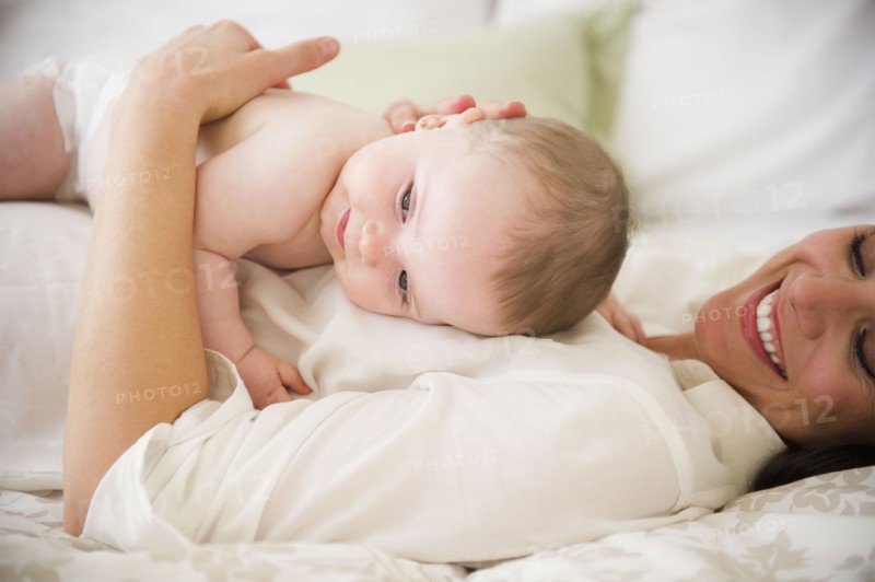 Mother with baby daughter (6-11 months) lying on bed. 
Photo: Jamie Grill