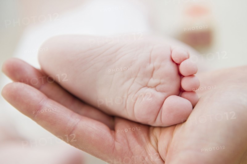 Close up of mother's hand holding baby daughter's (6-11 months) foot. 
Photo : Jamie Grill