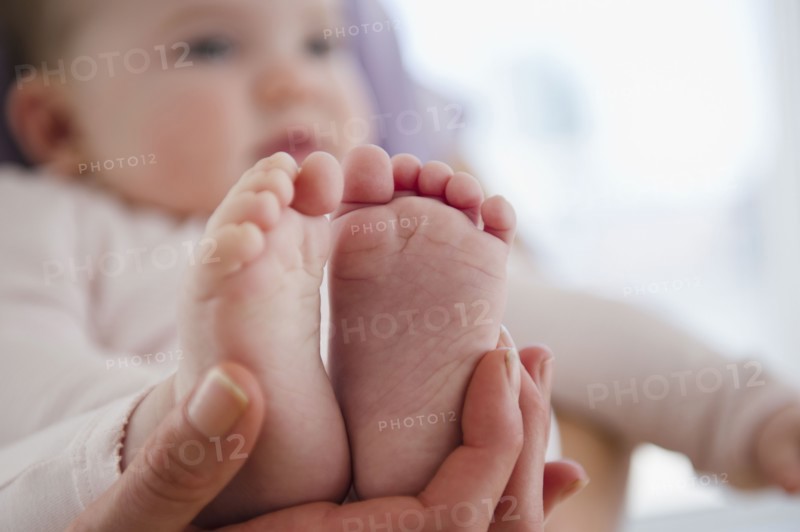 Close up of mother's hand holding baby daughter's (6-11 months) feet. 
Photo : Jamie Grill