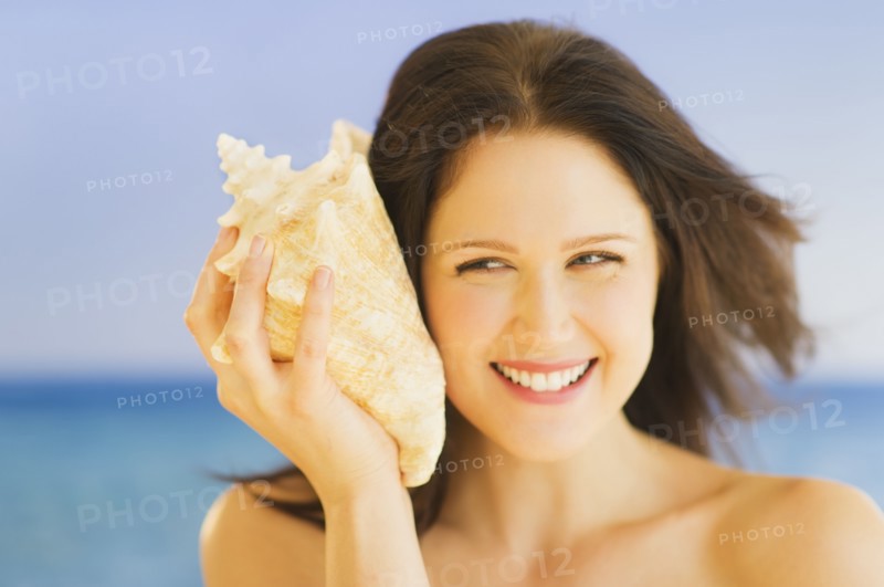 Portrait of young woman listening to seashell, studio shot. 
Photo: Daniel Grill