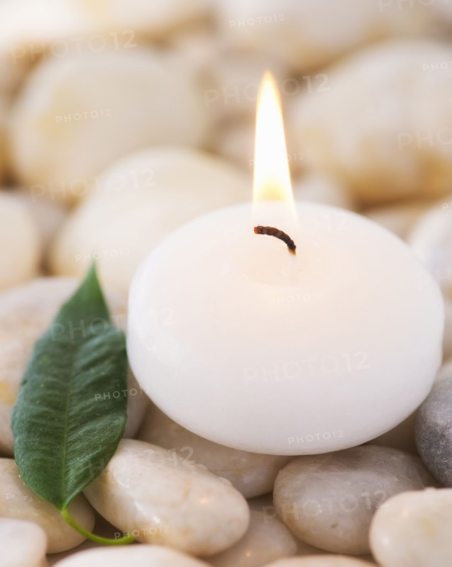 Close up of tea light and green leaf on pebble stones, studio shot. 
Photo: Daniel Grill