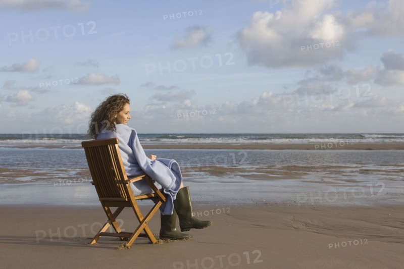 France, Pas-de-Calais, Escalles, Young woman sitting on chair on empty beach. 
Photo: Jan Scherders