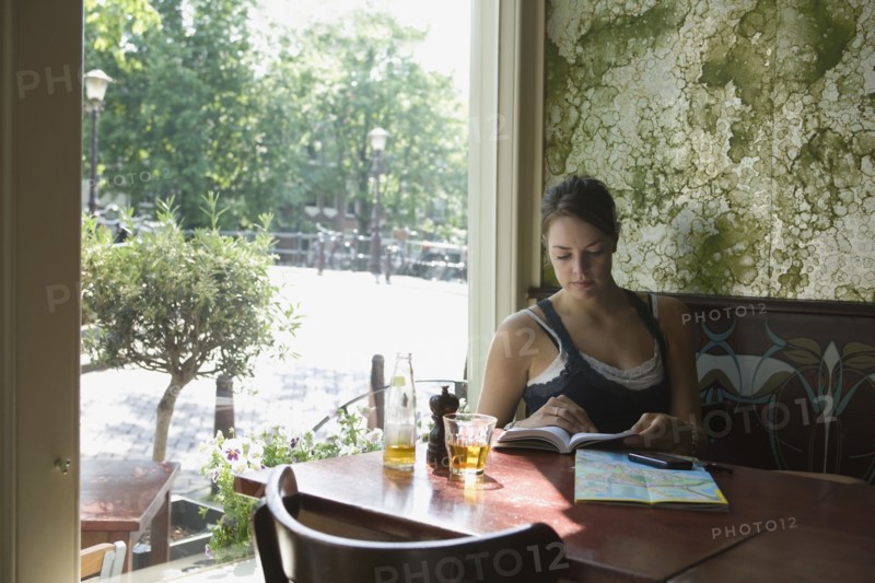 Holland, Amsterdam, Woman sitting with book in cafe window. 
Photo : Jan Scherders