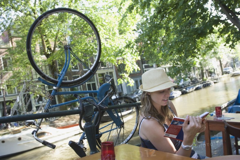 Holland, Amsterdam, Woman with guidebook sitting by canalside. 
Photo : Jan Scherders