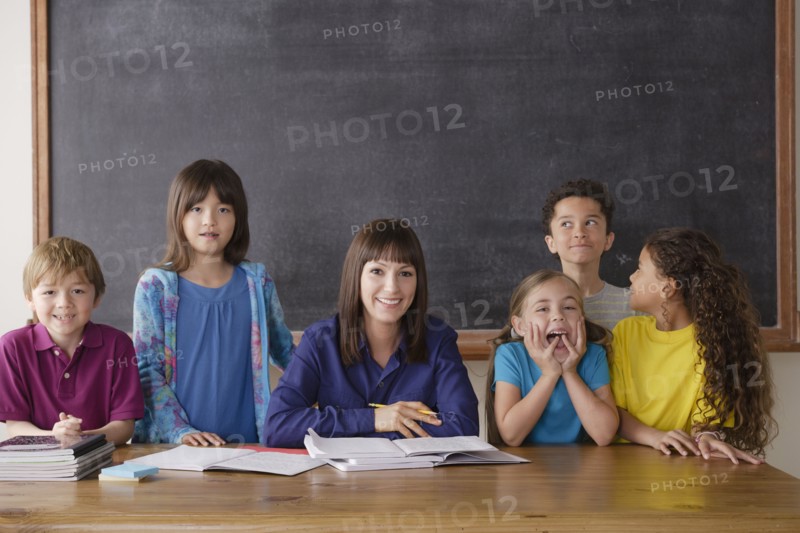 Teacher sitting by desk with group of pupils. 
Photo: Rob Lewine