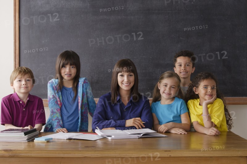 Teacher sitting by desk with group of pupils. 
Photo: Rob Lewine