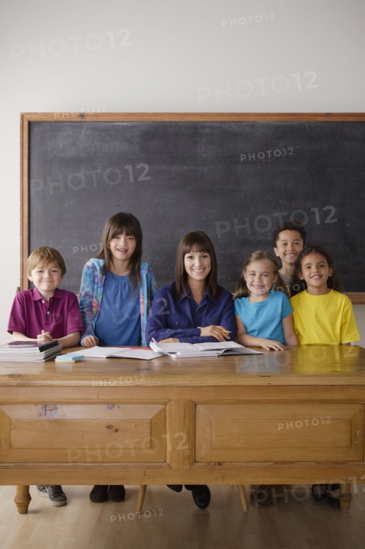 Teacher sitting by desk with group of pupils. 
Photo: Rob Lewine