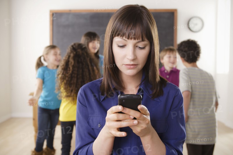 Teacher using mobile phone with group of pupils in background. 
Photo: Rob Lewine