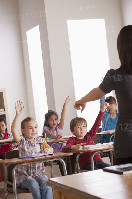 Pupils in classroom raising hands. 
Photo: Rob Lewine
