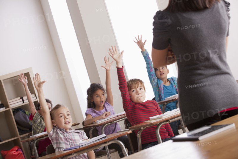 Pupils in classroom raising hands. 
Photo: Rob Lewine