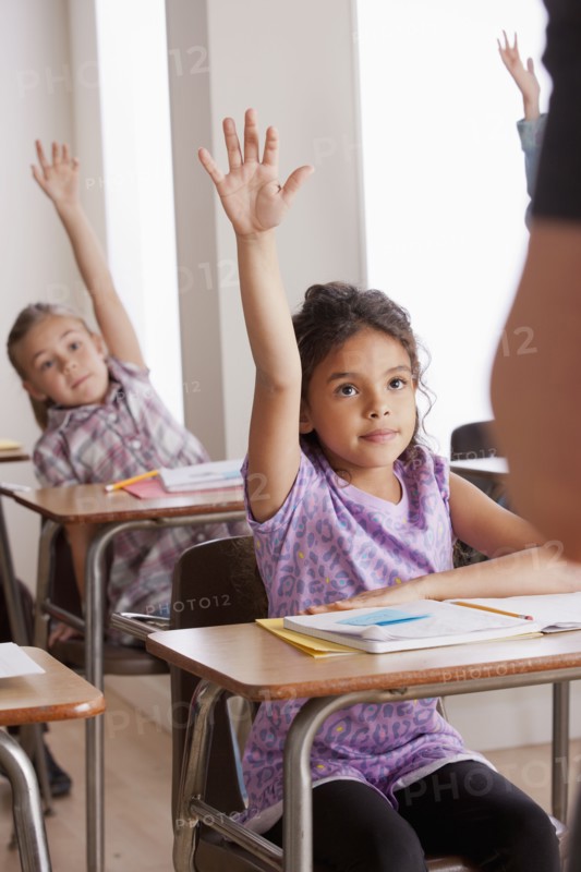 Pupils in classroom raising hands. 
Photo: Rob Lewine