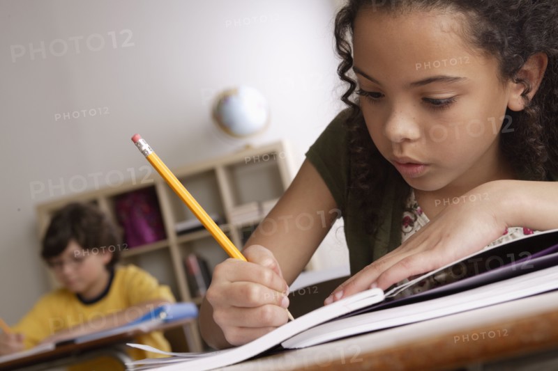 Writing girl (10-11) with boy (10-11) in background. 
Photo : Rob Lewine
