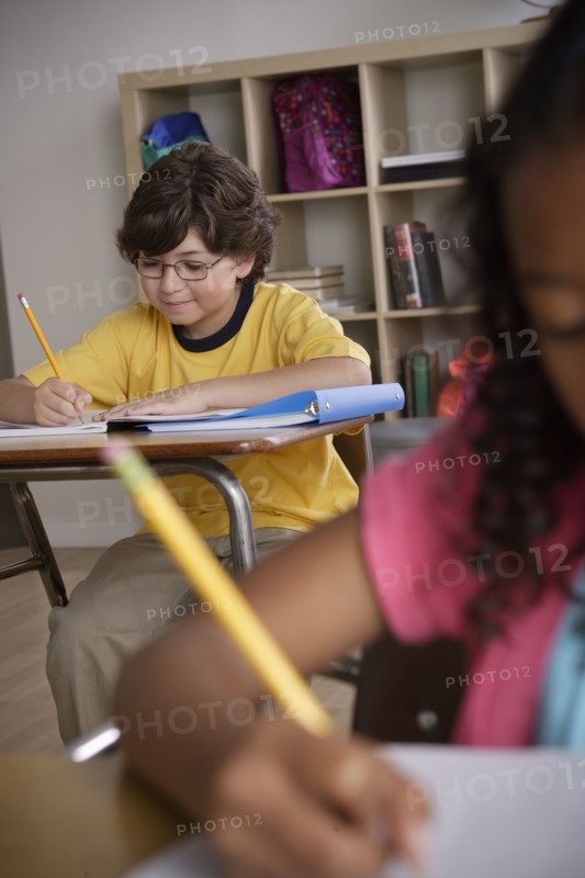Writing boy (10-11) with girl (10-11) in foreground. 
Photo : Rob Lewine