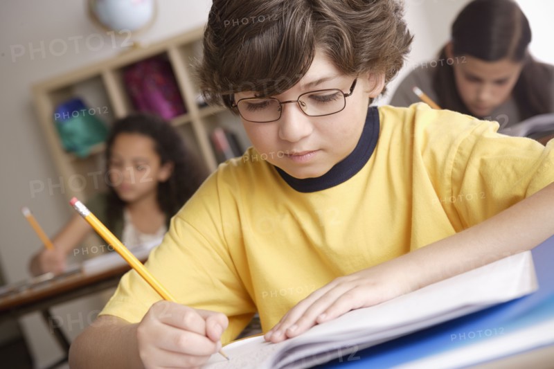 Writing boy (10-11) with girls (10-11, 12-13) in background. 
Photo : Rob Lewine