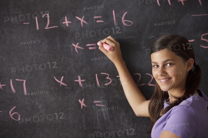 Portrait of schoolgirl (12-13) standing in front of blackboard during math classes. 
Photo : Rob Lewine
