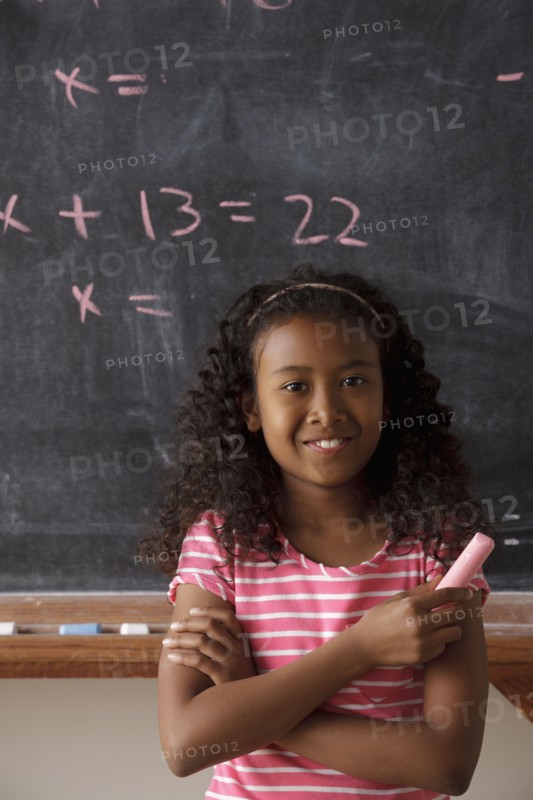 Portrait of schoolgirl (10-11) standing in front of blackboard during math classes. 
Photo: Rob Lewine