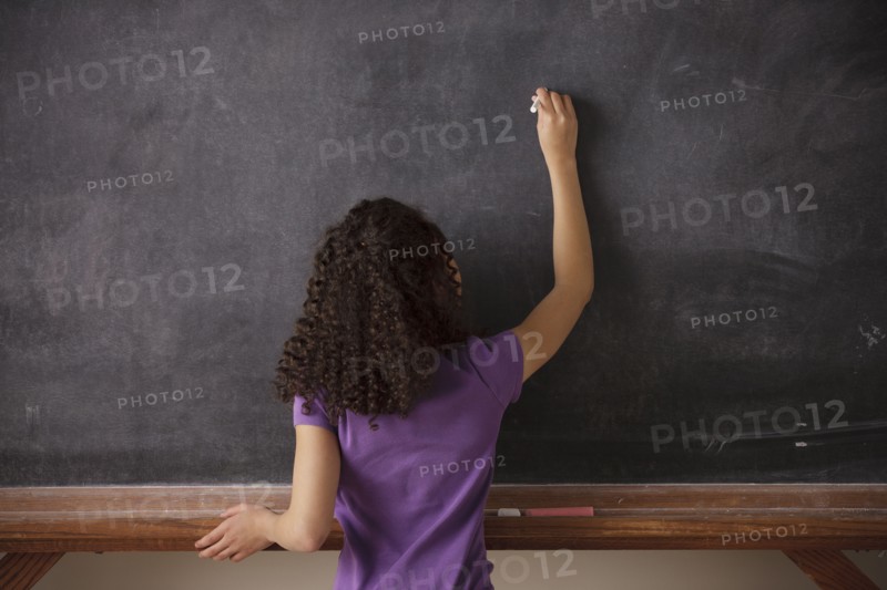 Portrait of schoolgirl (10-11) writing on blackboard. 
Photo : Rob Lewine