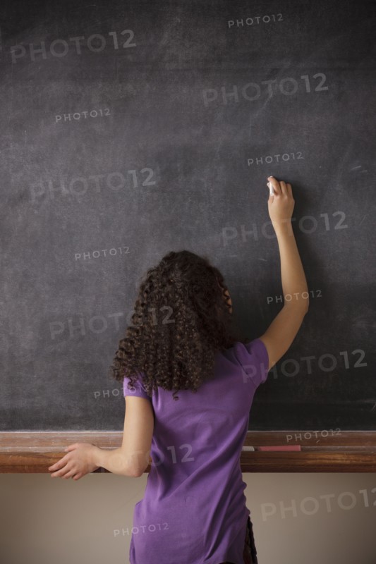 Portrait of schoolgirl (10-11) writing on blackboard. 
Photo : Rob Lewine