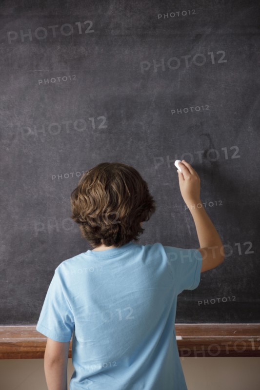 Rear view of schoolboy (10-11) writing on blackboard. 
Photo : Rob Lewine
