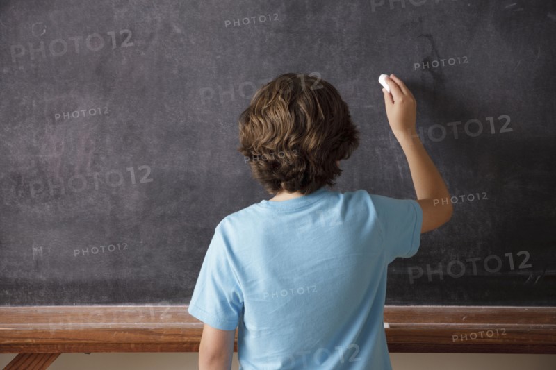 Rear view of schoolboy (10-11) writing on blackboard. 
Photo : Rob Lewine