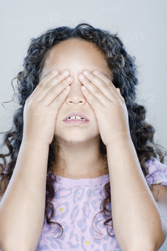 Girl (8-9) covering her eyes, studio shot. 
Photo: Rob Lewine