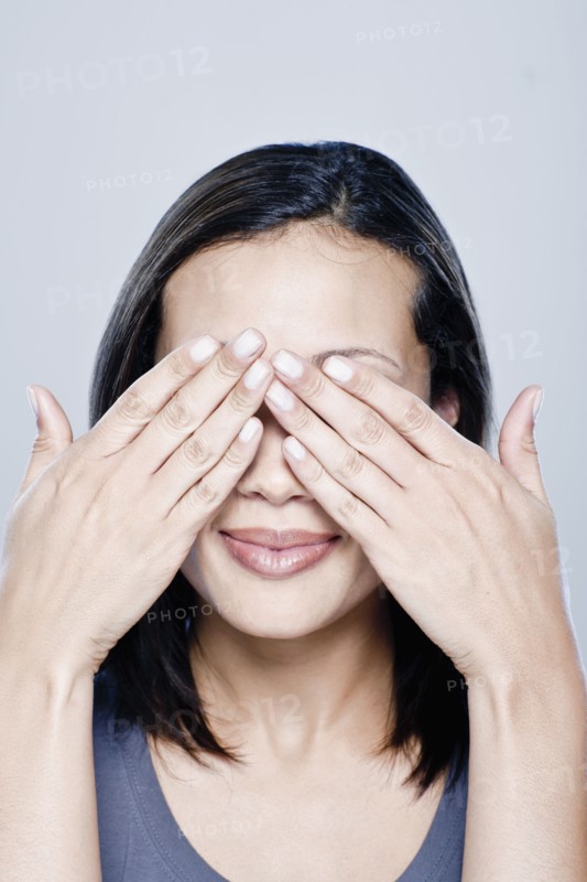 Portrait of young woman with hands covering eyes, studio shot. 
Photo : Rob Lewine