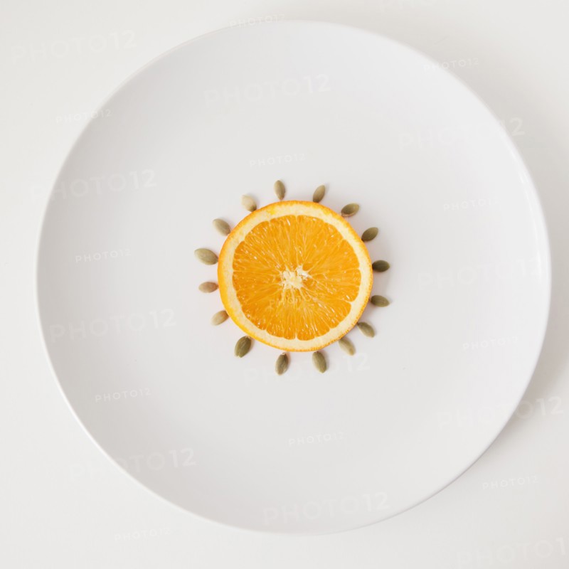 Slice of orange and seeds on plate, studio shot. 
Photo : Jessica Peterson