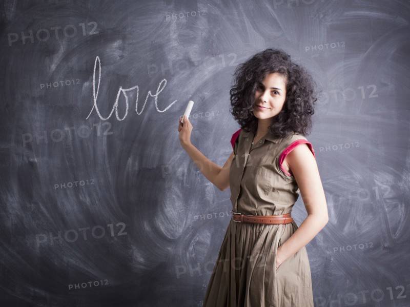 Young teacher posing against blackboard with word love written on it. 
Photo : Jessica Peterson