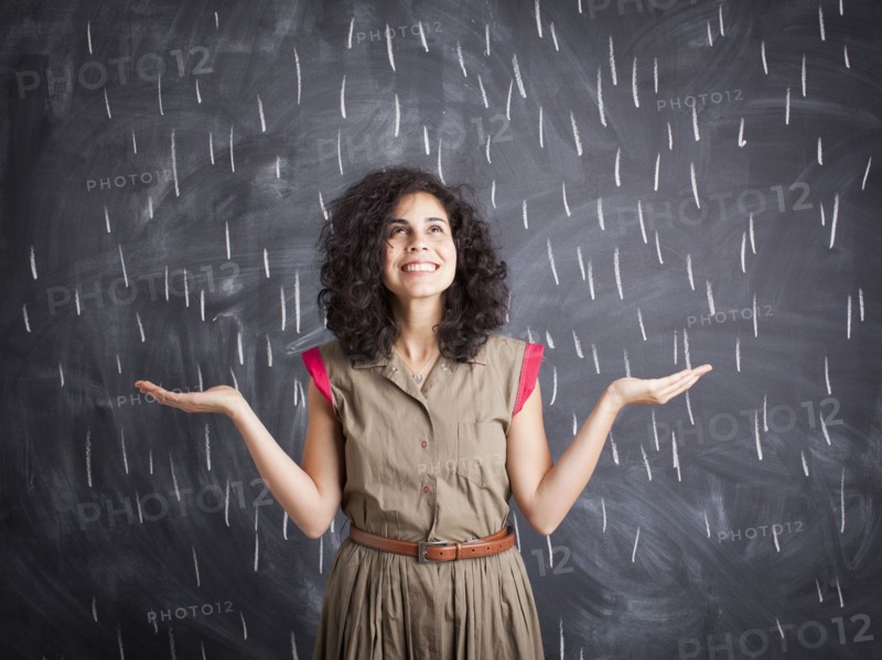 Young teacher posing against blackboard with V marks imitating rain. 
Photo: Jessica Peterson