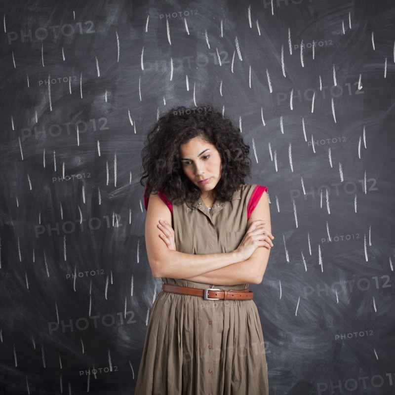 Young depressed teacher posing against blackboard with V marks imitating rain. 
Photo : Jessica Peterson