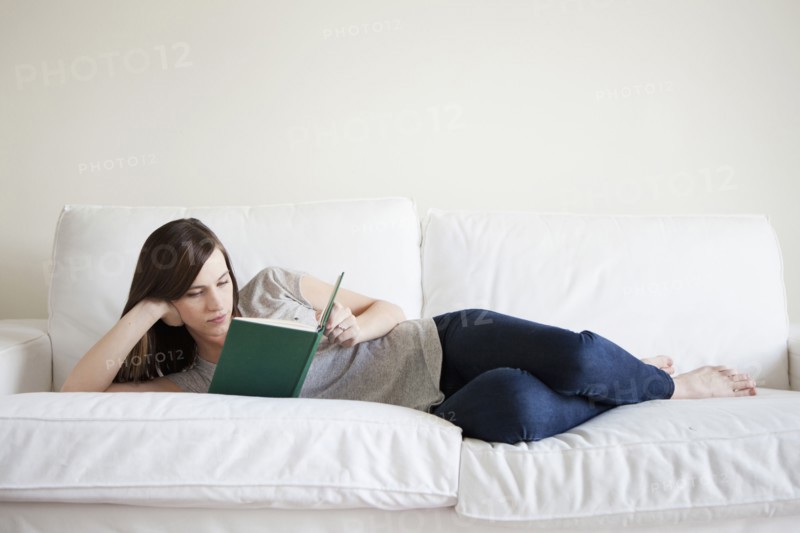 Young woman reclining on bed, reading book. 
Photo: Jessica Peterson