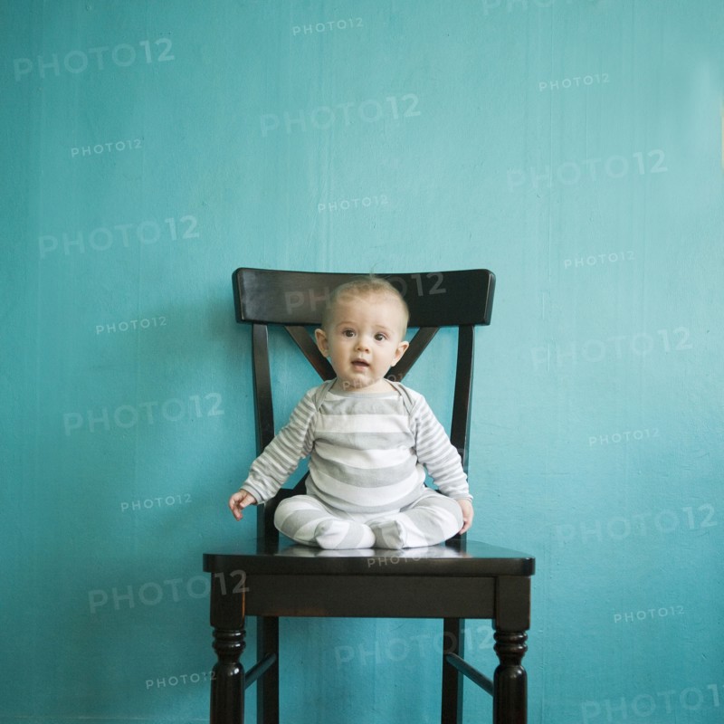Toddler boy (2-3) sitting on tall chair on blue background. 
Photo : Jessica Peterson