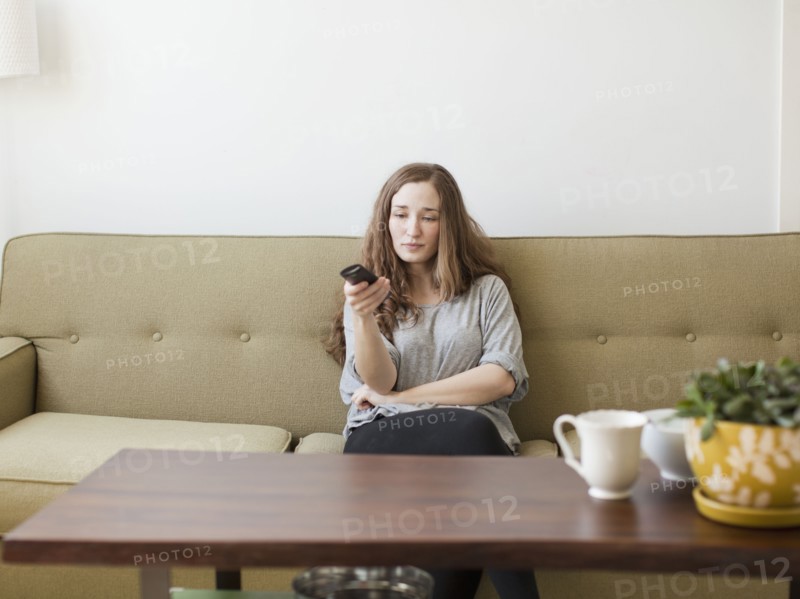 Bored young woman sitting on sofa with remote control. 
Photo : Jessica Peterson