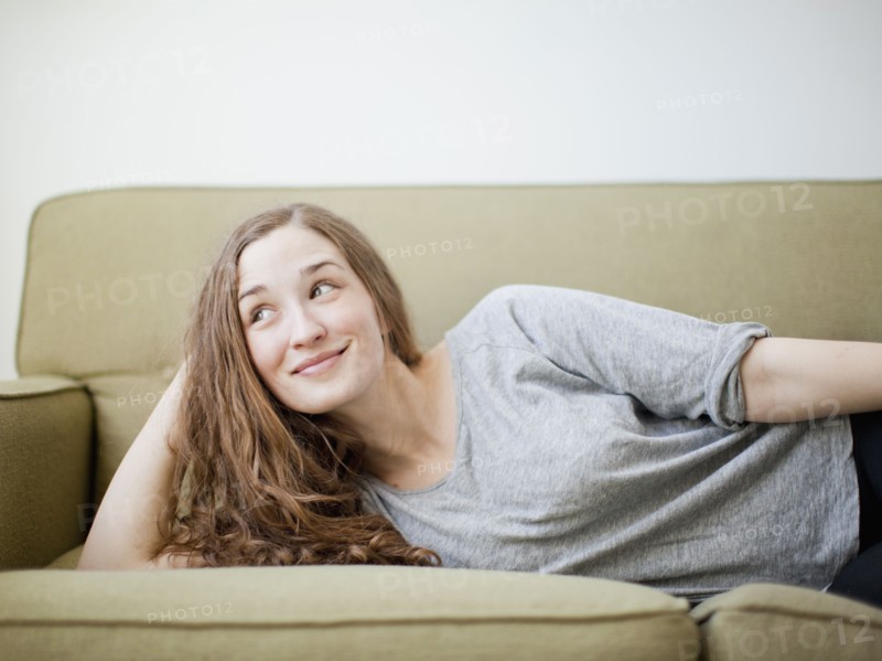 Happy young woman reclining on sofa. 
Photo : Jessica Peterson
