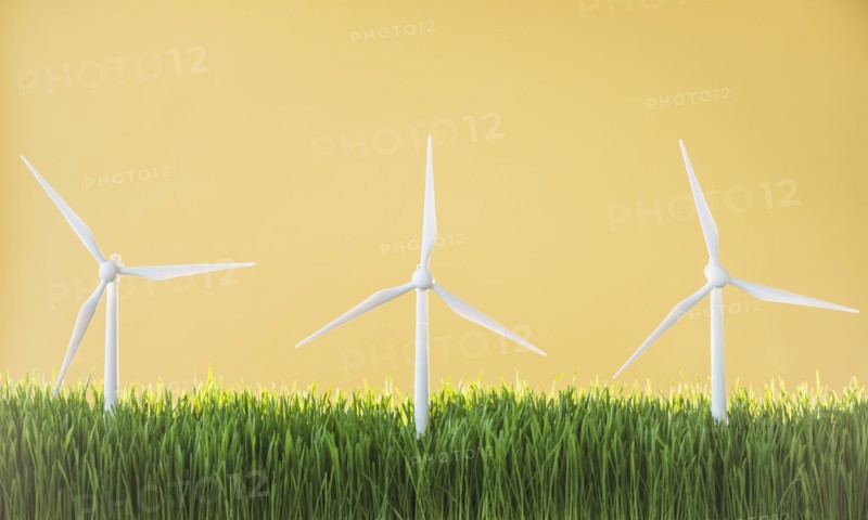 Model wind turbines in grass on yellow background.