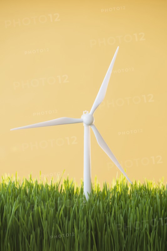 Model wind turbines in grass on yellow background.