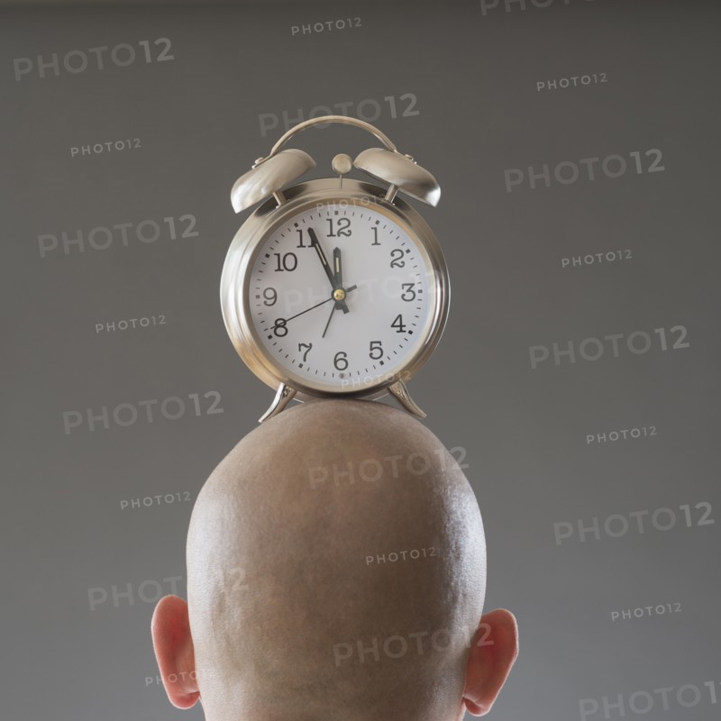Back view of man with alarm clock on shaved head.