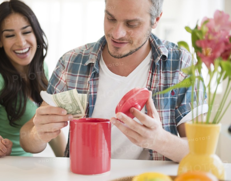 Couple putting money in savings jar. Photo: Jamie Grill