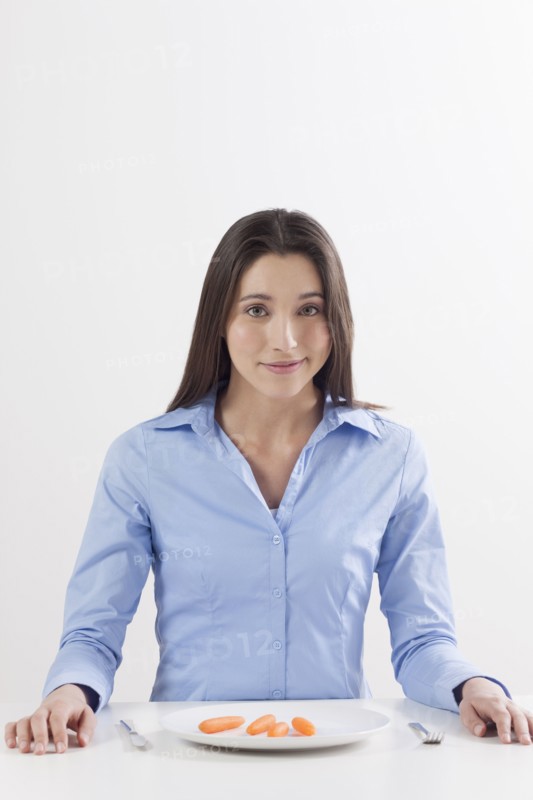 Studio shot of woman with baby carrots on plate. Photo: Jan Scherders