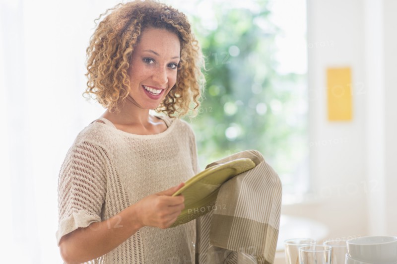 Young woman drying plates in kitchen.
