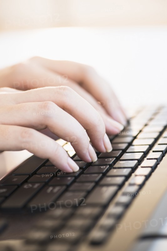 Close up of woman's hands typing on computer keyboard .