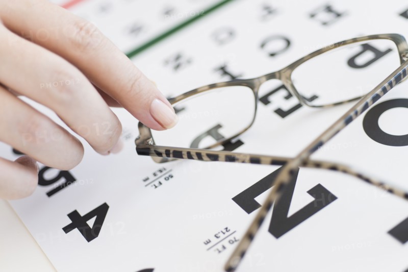 Close up of woman's hands holding glasses above eye chart, studio shot.