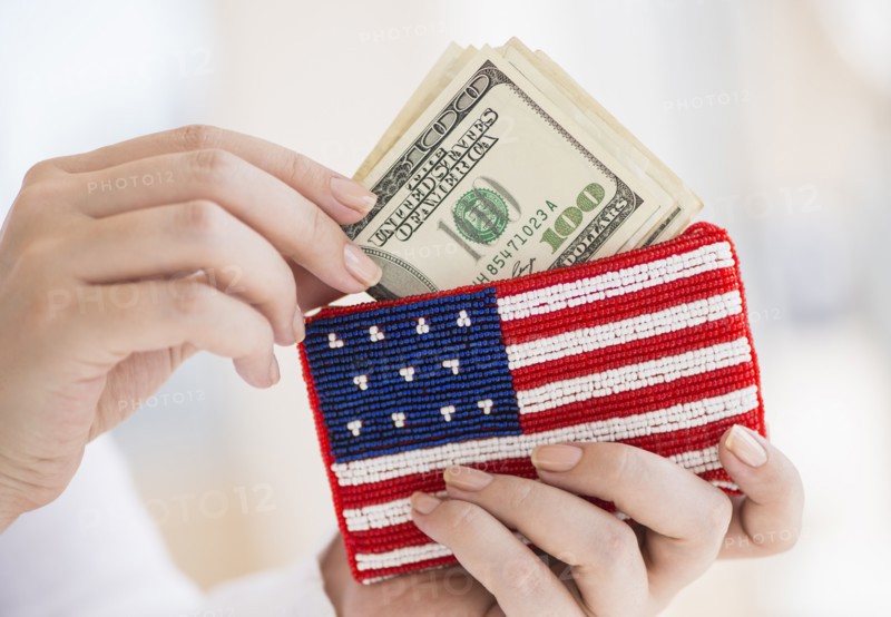 Woman holding banknotes and purse with american flag on it.