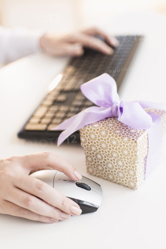 Gift box on desk next to woman using computer.