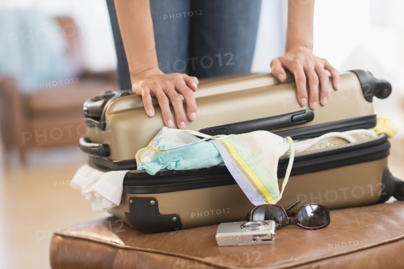 Woman trying to close full suitcase.