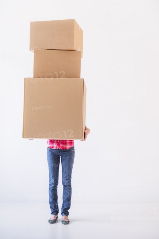 Studio shot of young woman carrying stack of boxes. Photo : Daniel Grill