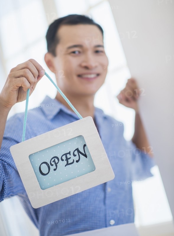 Mid adult waiter holding open sign. Photo: Daniel Grill