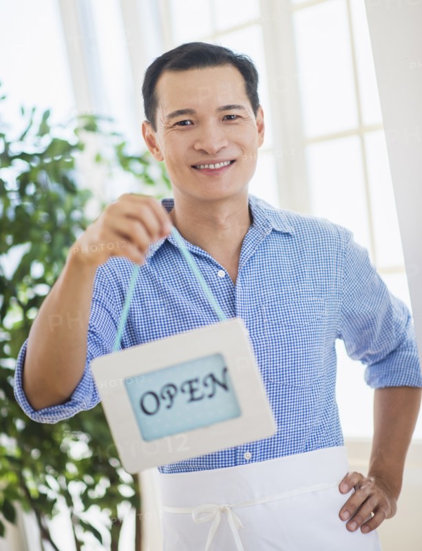 Mid adult waiter holding open sign. Photo : Daniel Grill