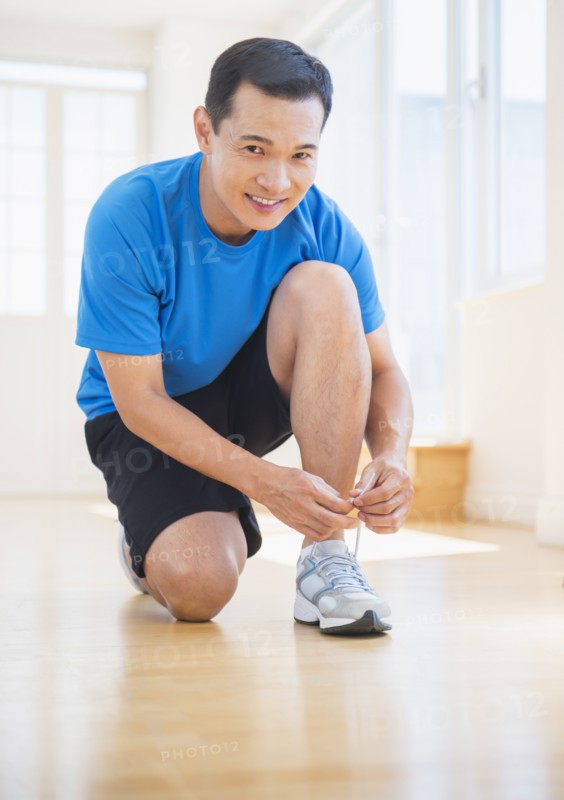 Mid adult man lacing his running shoes. Photo : Daniel Grill